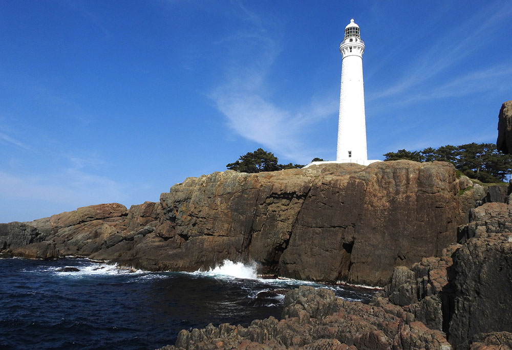 出雲ひのみさき灯台と柱状節理の拡大写真。出雲ひのみさき灯台は、100年以上の歴史をもつ高さ約44メートルの白い塔で、石造りの灯台としては日本一の高さを誇ります。この灯台の周辺を含むひのみさき周辺の海岸は「柱状節理」と呼ばれる火山性溶岩からなる四から六角形の形の規則的な断面をもつ岩が広がっています。